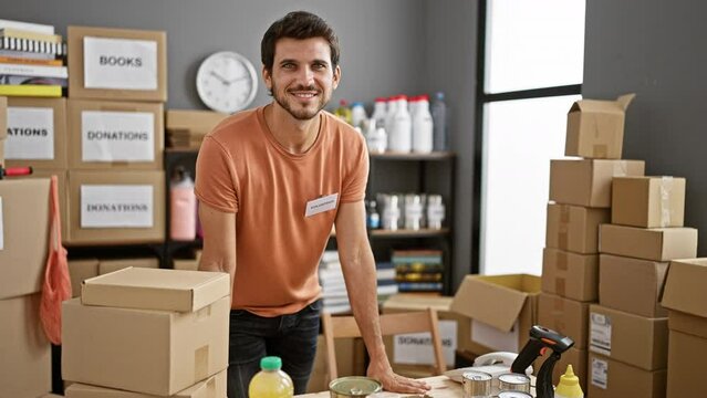 A young hispanic man with a beard volunteers in an indoor donation center, organizing boxes and goods.