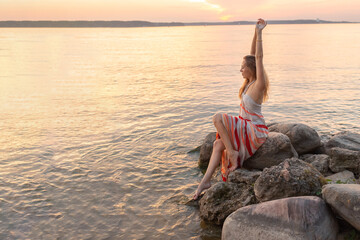 a girl sits on large stones on a beautiful sea coast. vacation by the sea