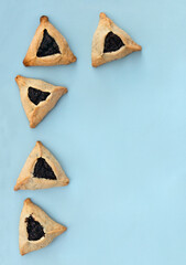 Triangular cookies with poppy seeds ( hamantasch or aman ears ) for jewish holiday of purim celebration on blue background with space for text. Top view, flat lay - obrazy, fototapety, plakaty