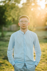 Male portrait on summer day closeup. A handsome man in glasses stands on green grass at sunset. Serious male on the field in the sunset background.