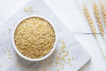 Dry bulgur wheat grains in bowl or spoon on table. Heap of uncooked bulghur , cereal food