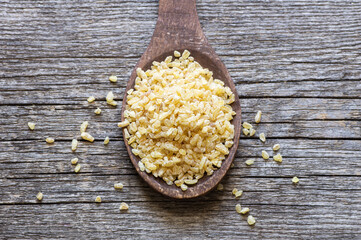 Dry bulgur wheat grains in bowl or spoon on table. Heap of uncooked bulghur , cereal food