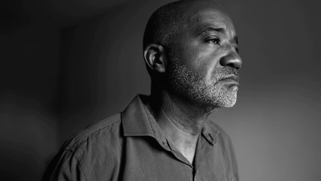 Aging Thoughtful African American senior man contemplating life's challenges in introspective silent mental reflection standing indoors by window in monochromatic black and white