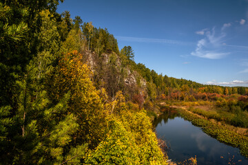 Obraz premium The river flows near the rocks covered with autumn forest.