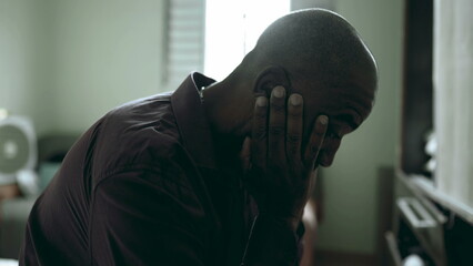 Close-up face of depressed senior struggles with life's challenges in moody gloomy bedroom covering face in shame and regret in somber atmosphere. African American person suffering