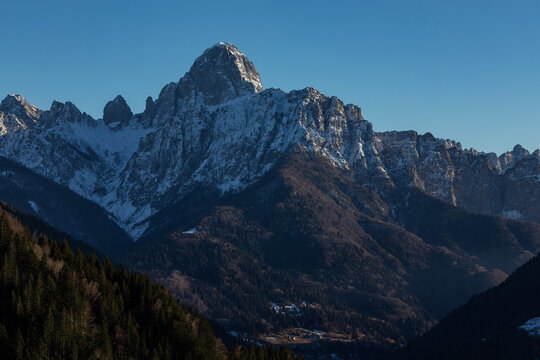 visuale in primo piano, del lato in ombra di una grande catena montuosa, in un ambiente naturale di montagna, parzialmente innevato, nelle alpi carniche nel nord-est Italia, al tramonto, in inverno