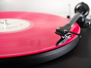 Closeup of a pink vinyl LP record on a turntable, with the tonearm needle or stylus positioned at the start of the first music track on one side of the album, ready to play.