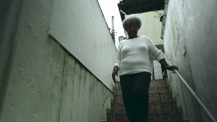 One elderly black lady from South American stepping out into sidewalk from residence. 80s female person of African descent going down the stairs and opens front door going out for daily routine