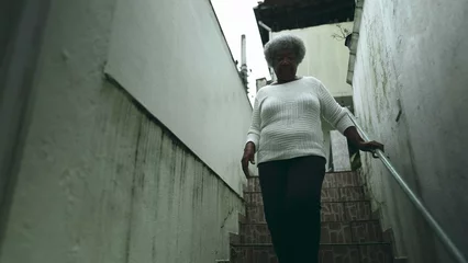 Cercles muraux Vielles portes One elderly black lady from South American stepping out into sidewalk from residence. 80s female person of African descent going down the stairs and opens front door going out for daily routine