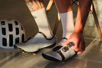 A male cyclist is putting on cycling shoes. Bicycle shoes with a modern system of tightening the...