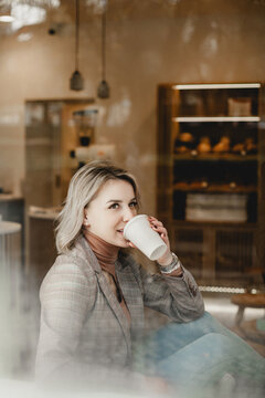 Cozy Cafe Moment. Woman Enjoying Coffee in Stylish Attire - Relaxing Cafe Ambiance with Woman in Jacket and Scarf Savoring Coffee - Casual Coffee Break in Comfortable Cafe Setting.