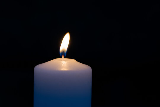 Simple white burning candle at night black background.