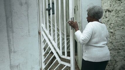 Elderly South American black woman arrives home from sidewalk street, opens residence front door...