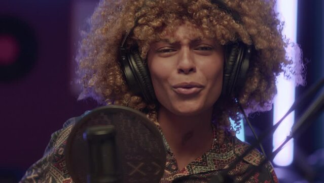 UGC closeup of cheerful African American lady with puffy hair singing song and having fun while recording music at home studio with neon lights at night