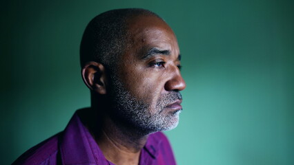 One pensive senior black man regretting past decision grimacing during challenging times standing indoors in isolation gazing at window, profile close-up face - obrazy, fototapety, plakaty