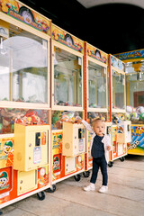 Little girl stands near a claw slot machine filled with toys