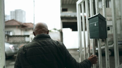 One senior black man going down the stairs and open front gate of residence in South America,...