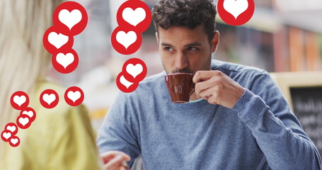 Image of heart icons floating over happy caucasian couple talking and drinking coffee