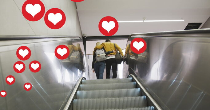 Image of heart icons floating over couple embracing on moving stairs - Powered by Adobe