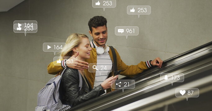 Image of social media icons floating over happy diverse couple embracing on moving stairs