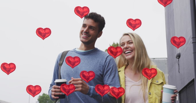 Image of heart icons floating over happy caucasian couple walking and drinking takeaway coffee