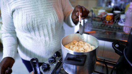 One elderly South American black woman standing in kitchen stove cooking pasta. Gray Haired 80s...