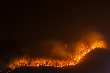 Orange forest fire rages in the mountains at night in Chiang Mai. It causes enormous amounts of...