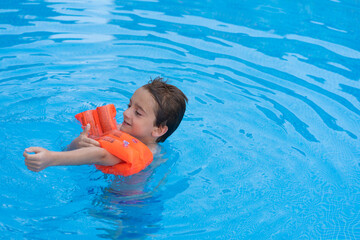 A child in a swimming pool while putting on orange life jackets.