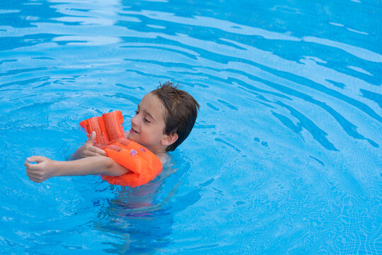 A Child In A Swimming Pool While Putting On Orange Life Jackets.