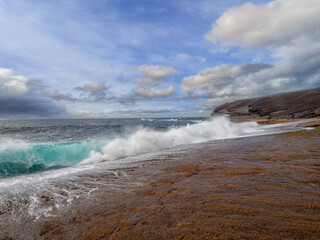 Fototapeta premium Powerful ocean wave hits rough stone coast. Blue cloudy sky. Warm sunny day. Kilkee area, Ireland. Popular tourist landmark with amazing nature scenery. Irish landscape.