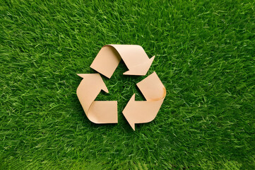 Recycling symbol cut out of kraft paper on green grass, top view, nature concept