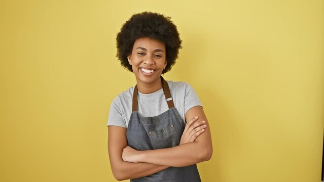 Confident african american woman, sporting a sunshine-yellow apron, smiles with pure joy! her arms are crossed assertively, radiating positivity against an isolated background.