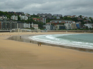 Obraz premium Beach landscape of the city of San Sebastián, País Vasco, Euskadi. Spain. Donostia. Tourists walking on the beach on a cloudy day.