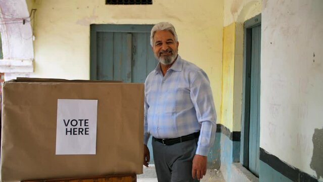 Grey-haired adult man casting his vote during elections through EVM - General elections  assembly elections. Old male happily giving his vote while doing a thumbs up gesture - right to vote  voting...