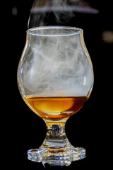 Glass of cognac with smoke against a dark backdrop