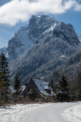 Snow covered road to Morskie Oko Lake with traditional wooden hut in the foreground and the high...