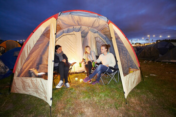 Happy woman, friends and night in tent at festival for party, event or carnival on outdoor campsite. Female person, people or group in relax or camping in the late evening with drinks and candlelight