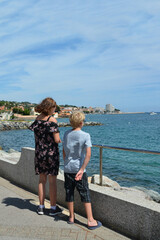 Two children stand on the promenade and look at the sea