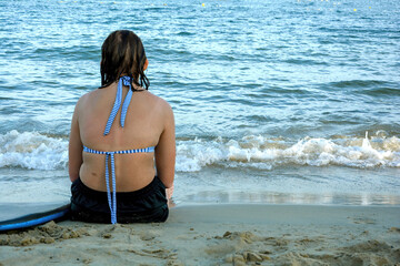 Girl from behind, sitting on the sandy beach by the sea