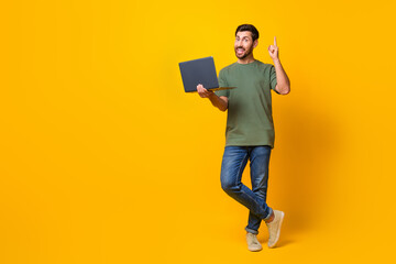 Full length photo of nice young male hold netbook point up brilliant idea wear trendy khaki garment isolated on yellow color background - obrazy, fototapety, plakaty