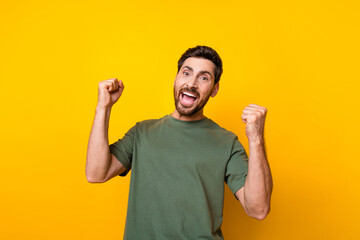 Photo of impressed funky guy dressed green t-shirt rising fists screaming yeah isolated yellow...