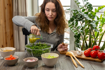 A woman pours dressing over rocket leaves and quinoa salad. Fresh homemade salad with arugula,...