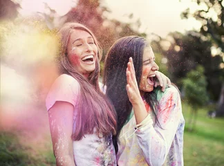 Tuinposter Happy, powder paint and girl friends laugh outdoor with Holi festival and colorful event with smile. Celebration, love and excited in nature with young people and crazy color dust for party together © peopleimages.com