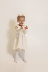 A little girl in a light full-length dress on a light background holds out her hands