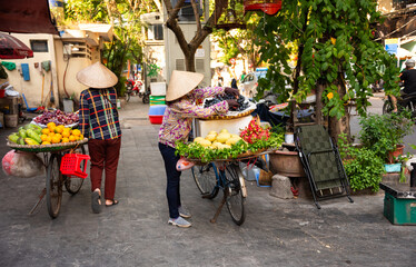 Vietnam street vendors. Woman with traditional Vietnamese hat selling fruit from bicycle in Hanoi