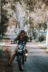 Chico con barba con atuendo de motorista posando con su moto y su cámara 