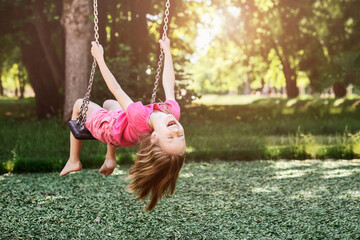 Children Holiday on Nature concept. Swing for Kids in Park. Smiling Child Having fun, Little Girl...