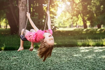 Fotobehang Children Holiday on Nature concept. Swing for Kids in Park. Smiling Child Having fun, Little Girl Swinging on Playground on Green Background Outside.  © Maryana