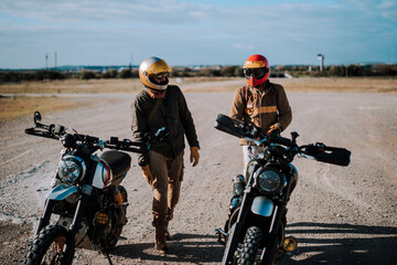 Dos amigos hombres con motos tipo scrambler en area desertica