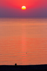 red sunrise at the black sea. sun above horizon on a cloudless sky. silhouette on the shore observing the beauty in nature